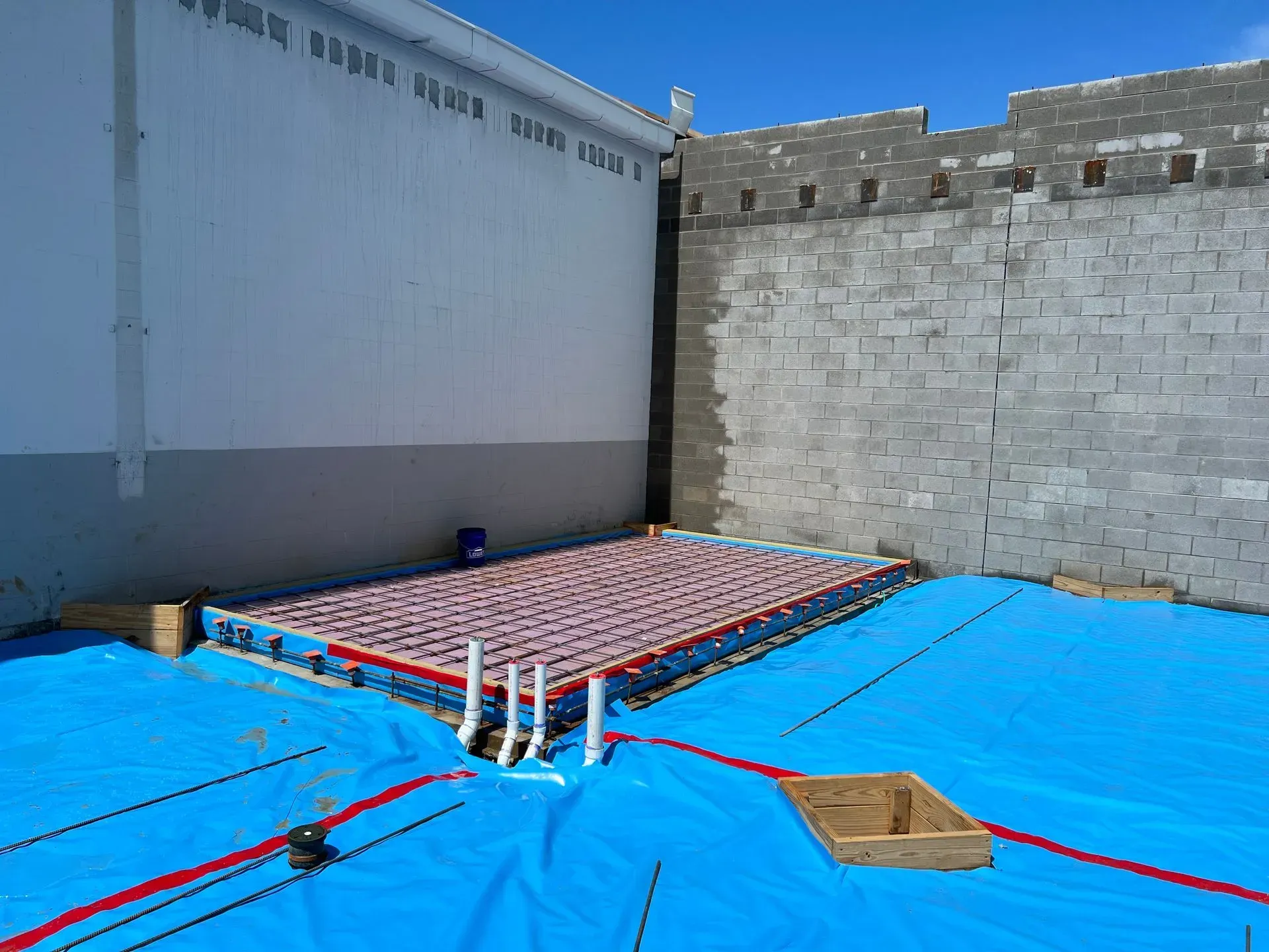 Construction site with a rectangular slab of red tubing for radiant heating atop a blue vapor barrier against grey walls.