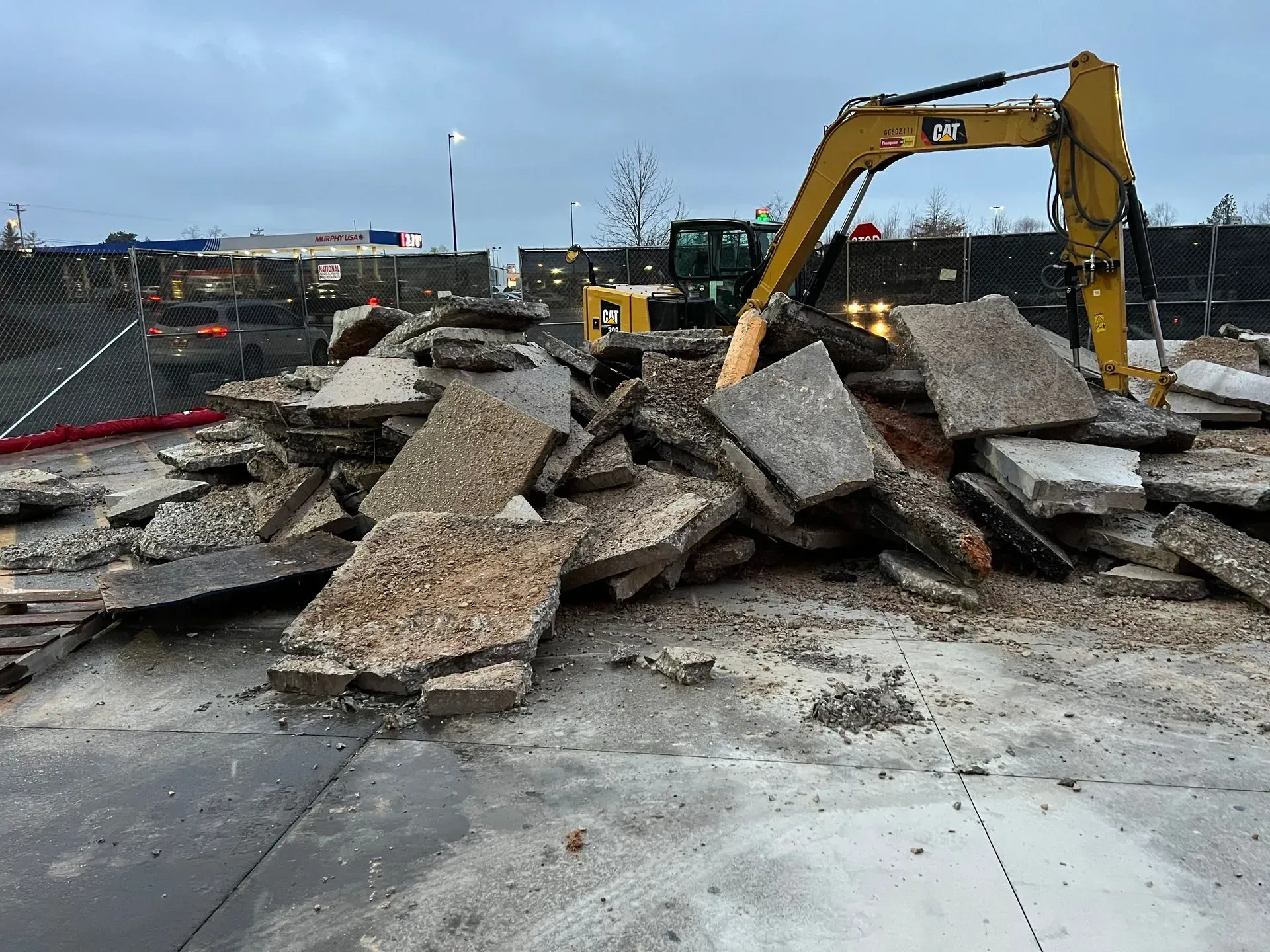 A yellow Caterpillar excavator parked behind a large pile of broken concrete slabs at a construction site.