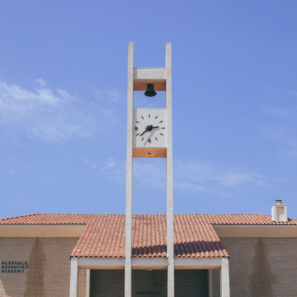 Clock tower with a bell on a tan building under a blue sky.