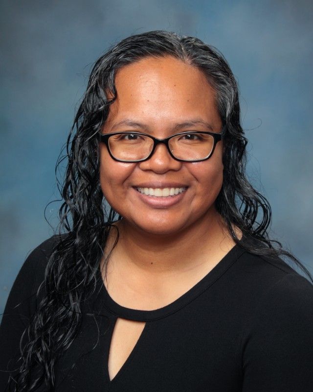 Woman with glasses and dark hair, smiling, wearing a black shirt with keyhole detail; blue background.