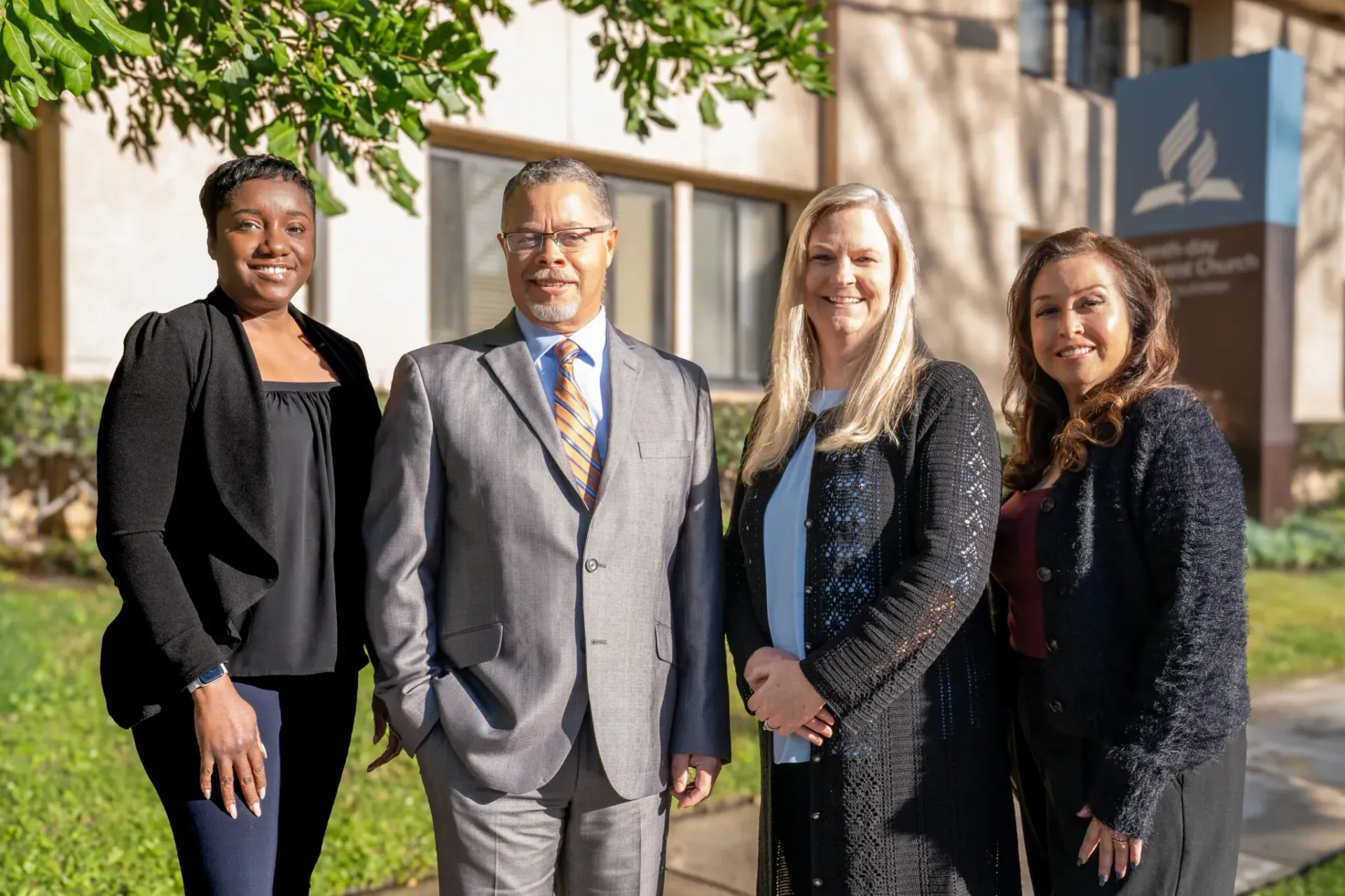 Four people standing in front of a building with a church sign.