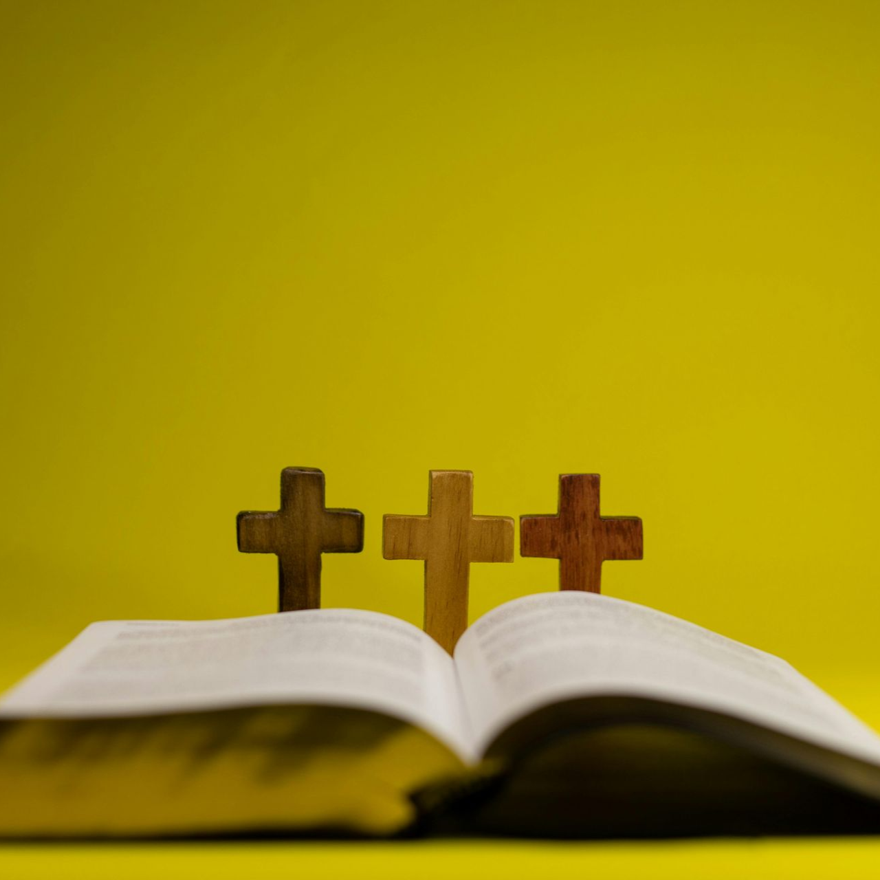 Open book with three wooden crosses against a yellow background.