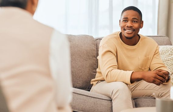 A man is sitting on a couch talking to another man.