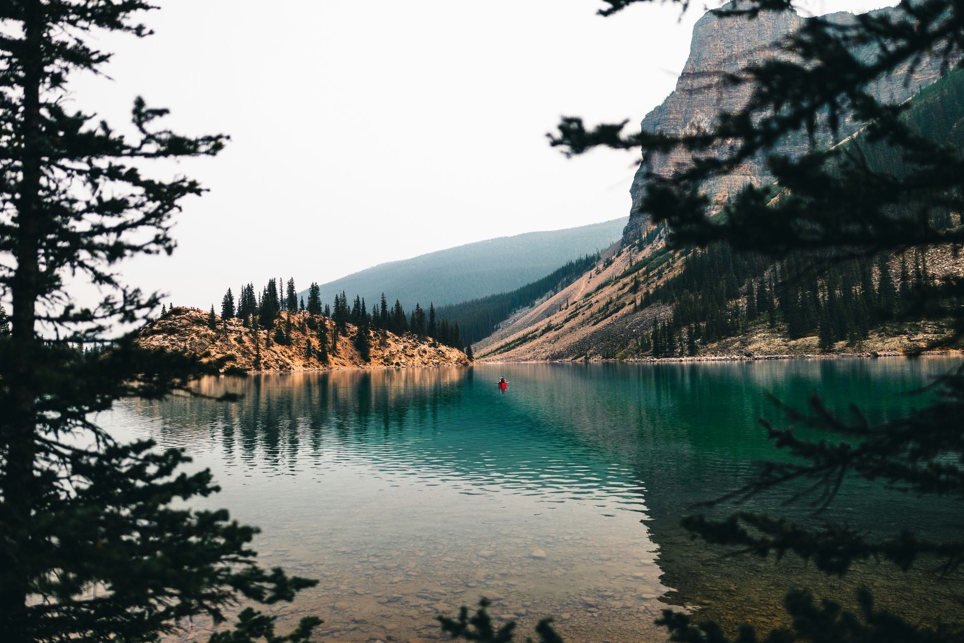 Turquoise lake with mountain backdrop, framed by dark trees.