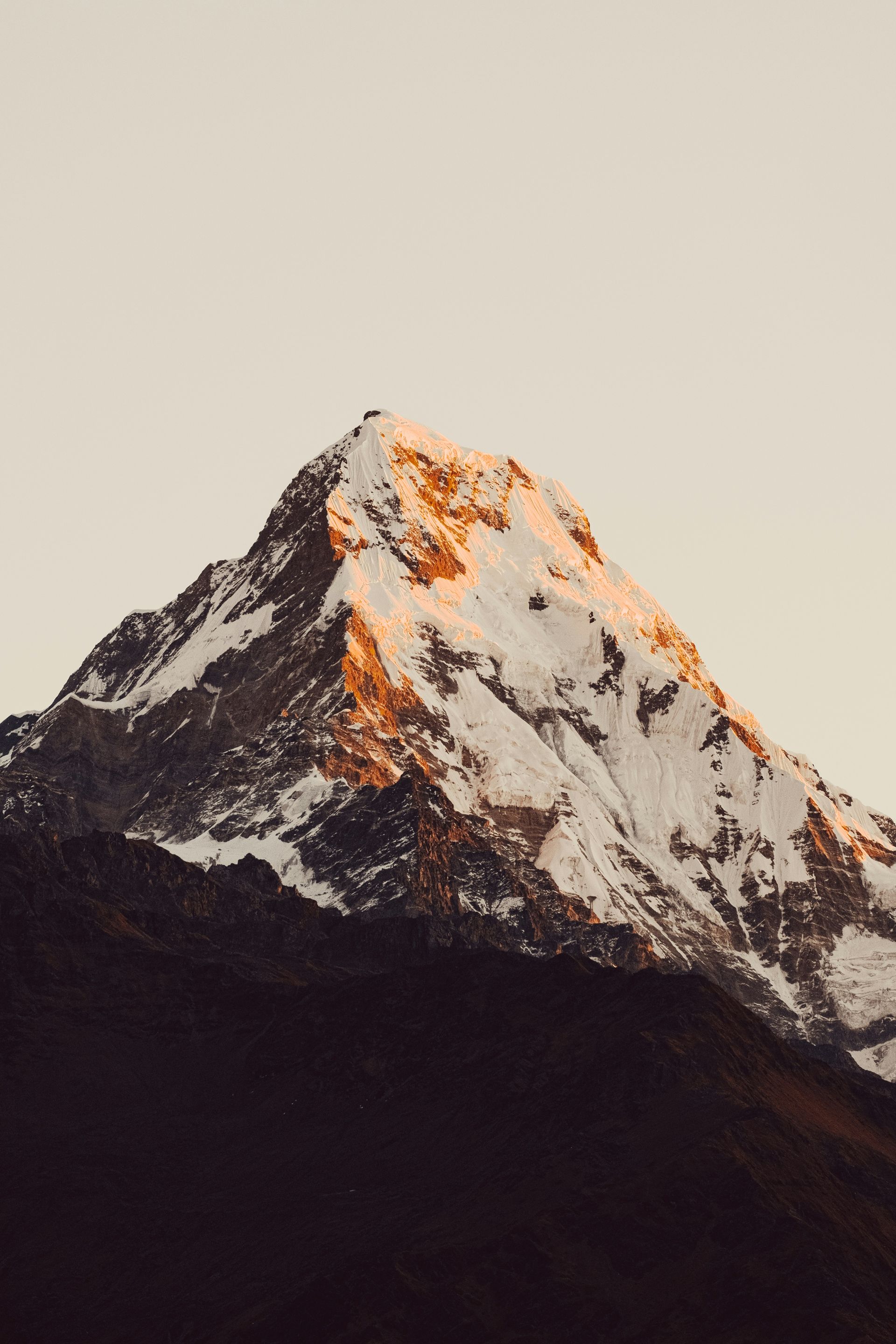 Snow-capped mountain peak lit by golden sunlight against a pale sky.