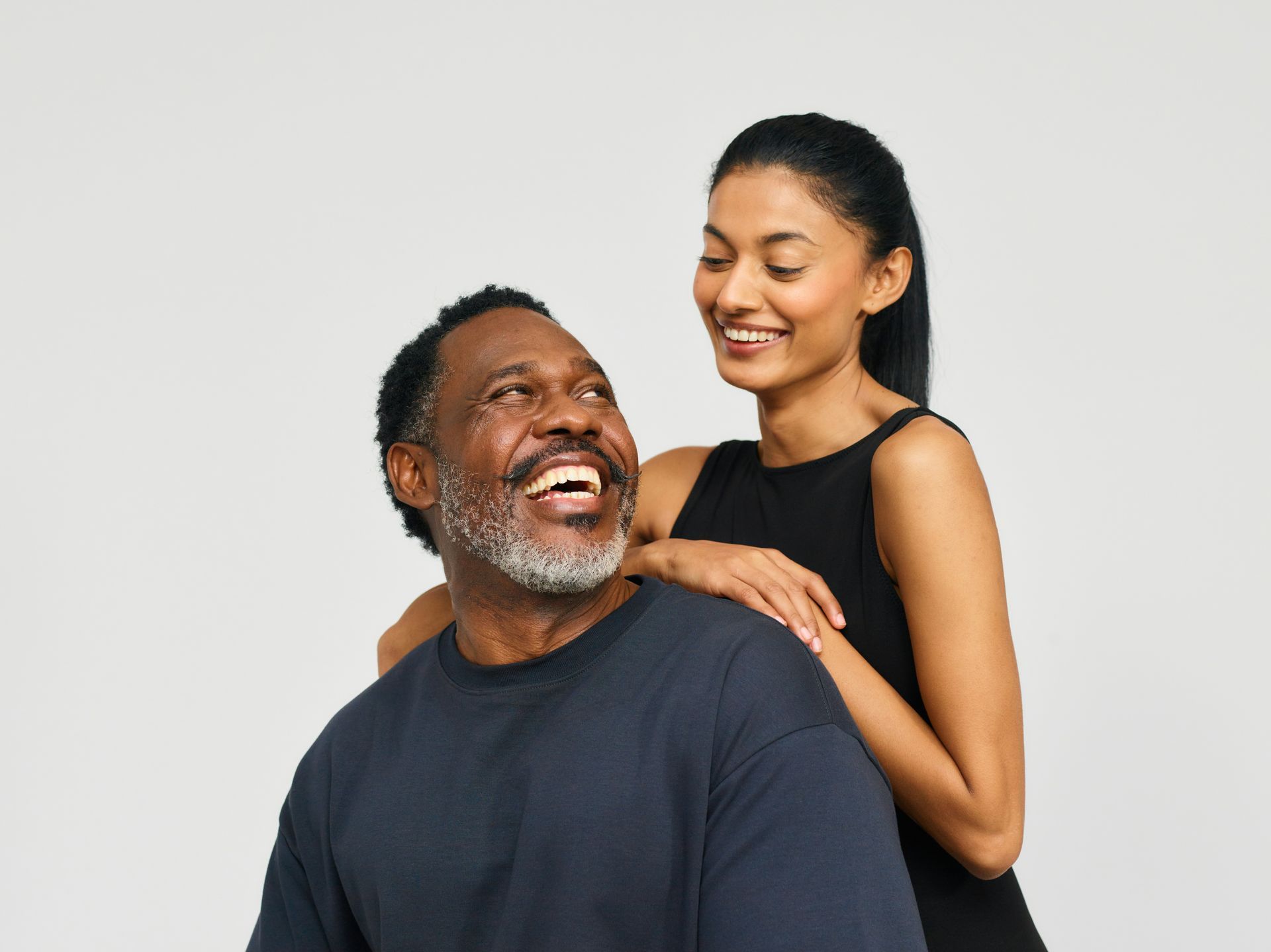 Woman smiling, arm on man's shoulder; both looking up and smiling against a white backdrop.