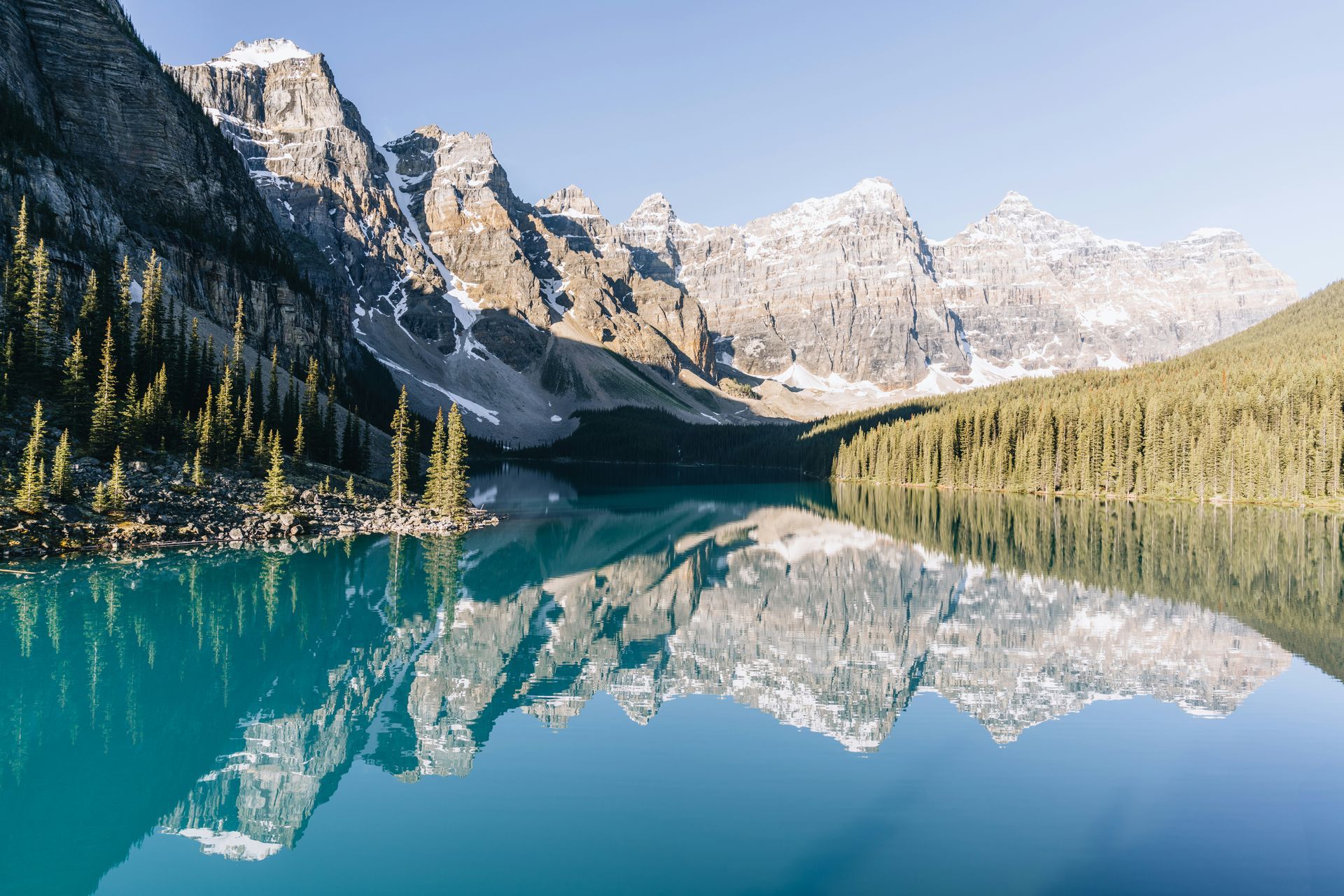 Emerald-blue lake reflects snow-capped mountains and evergreen trees in Banff National Park, Canada.