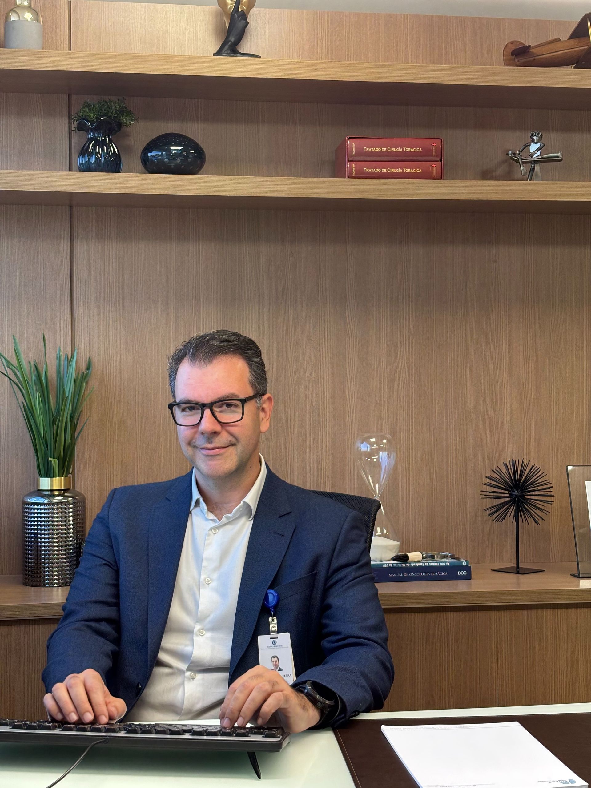 Um homem de terno está sentado em uma mesa em frente a um teclado de computador.