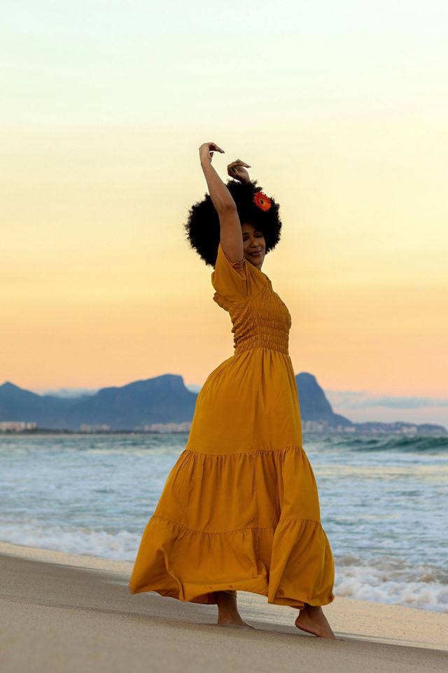 A woman in a yellow dress is standing on the beach.