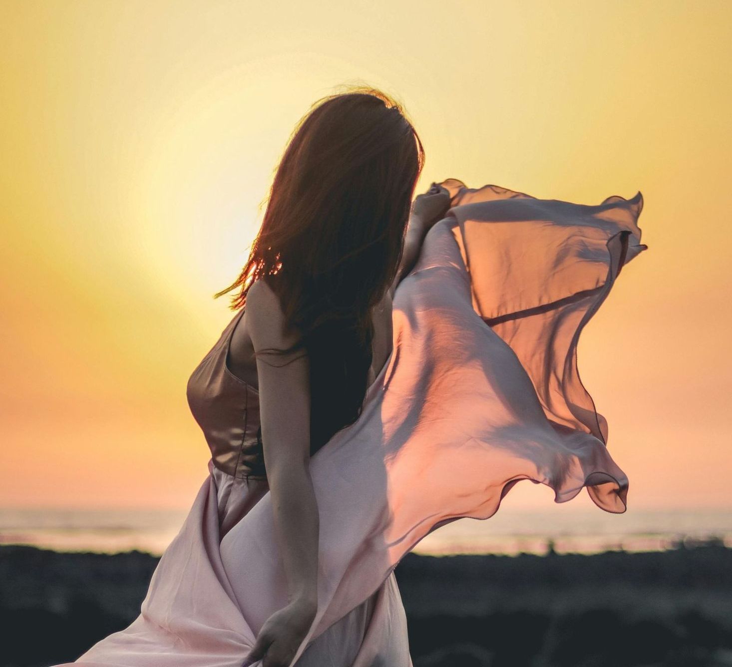 A woman in a white dress is standing in front of a sunset
