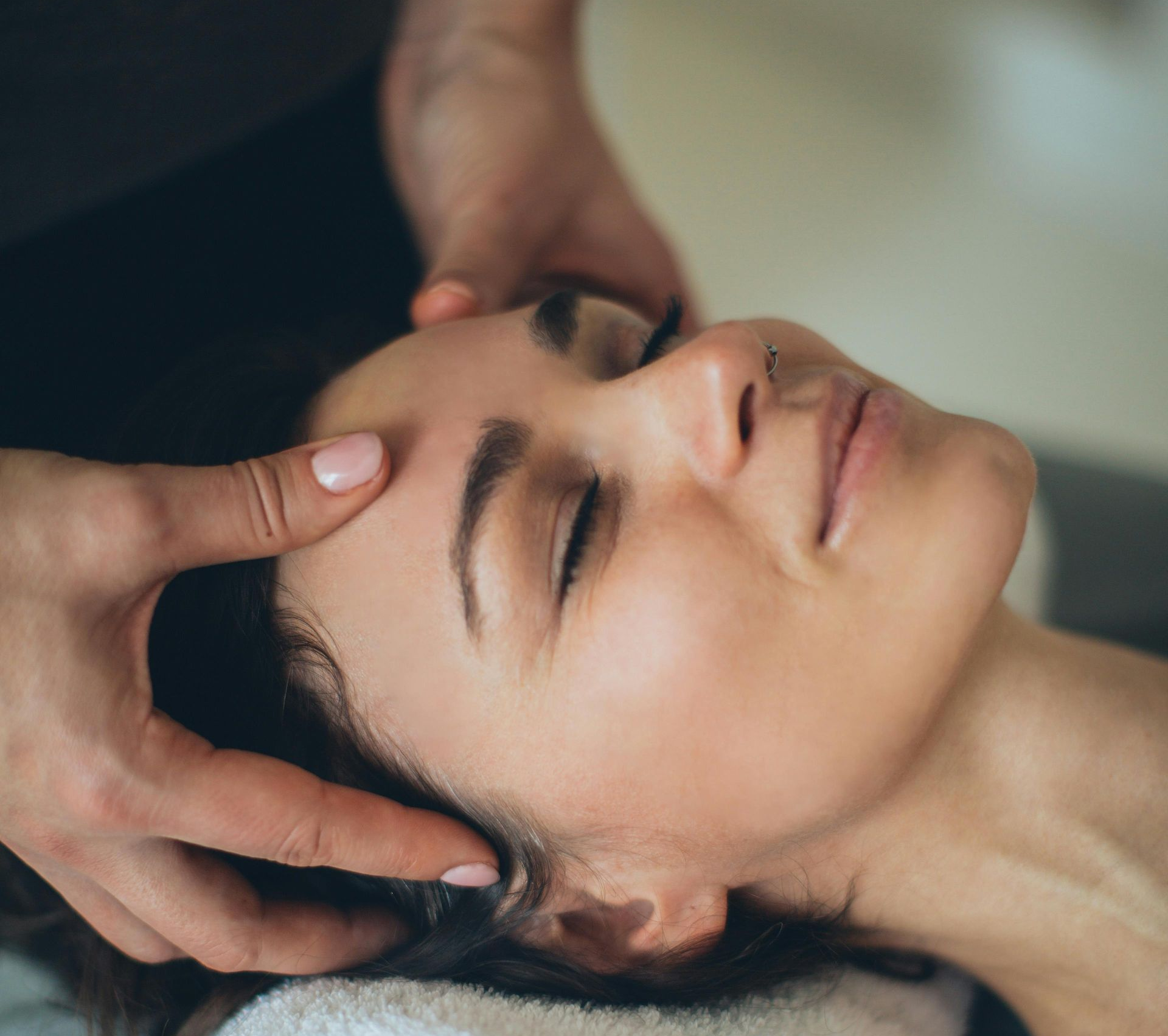Woman receiving a head massage with hands on her temples, eyes closed, in a spa-like setting.