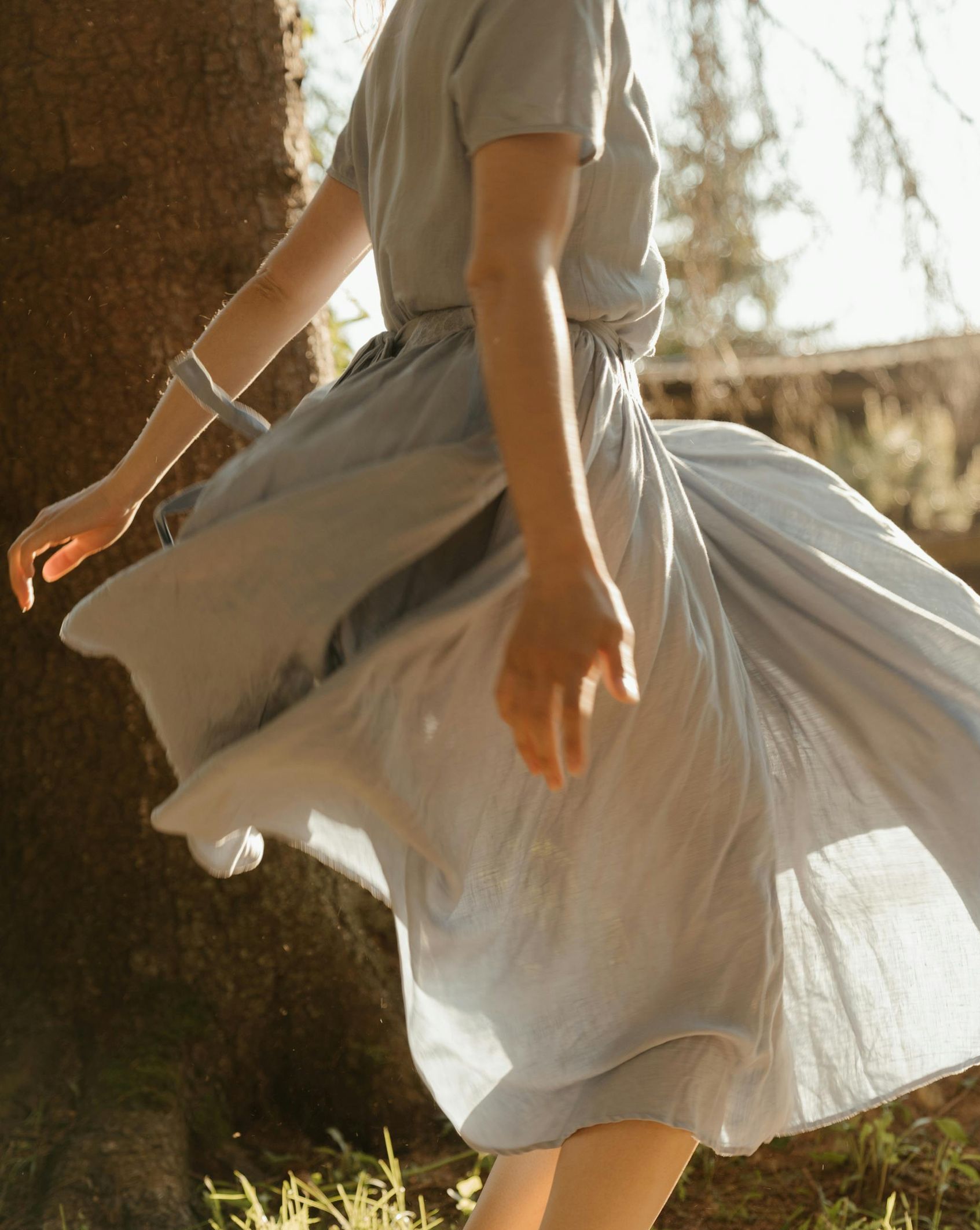 A woman in a white dress is dancing in front of a tree.