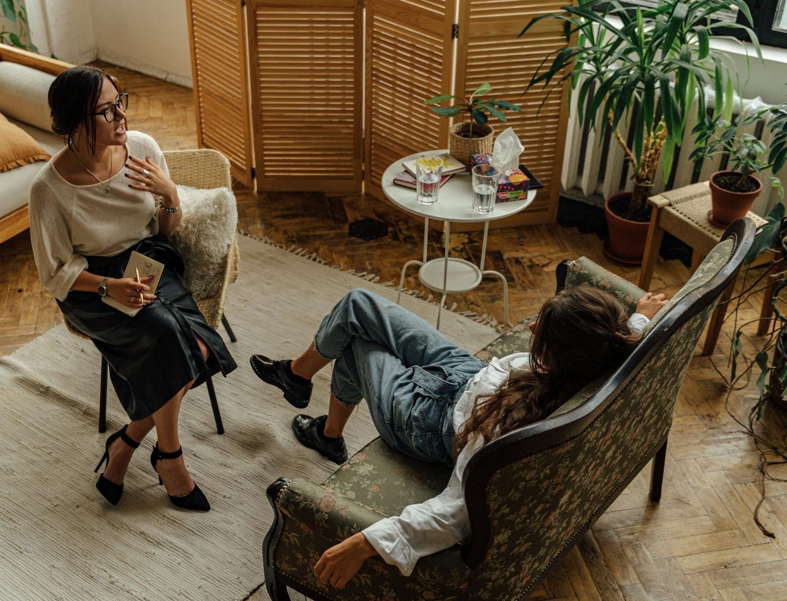 A woman is sitting on a couch talking to another woman.