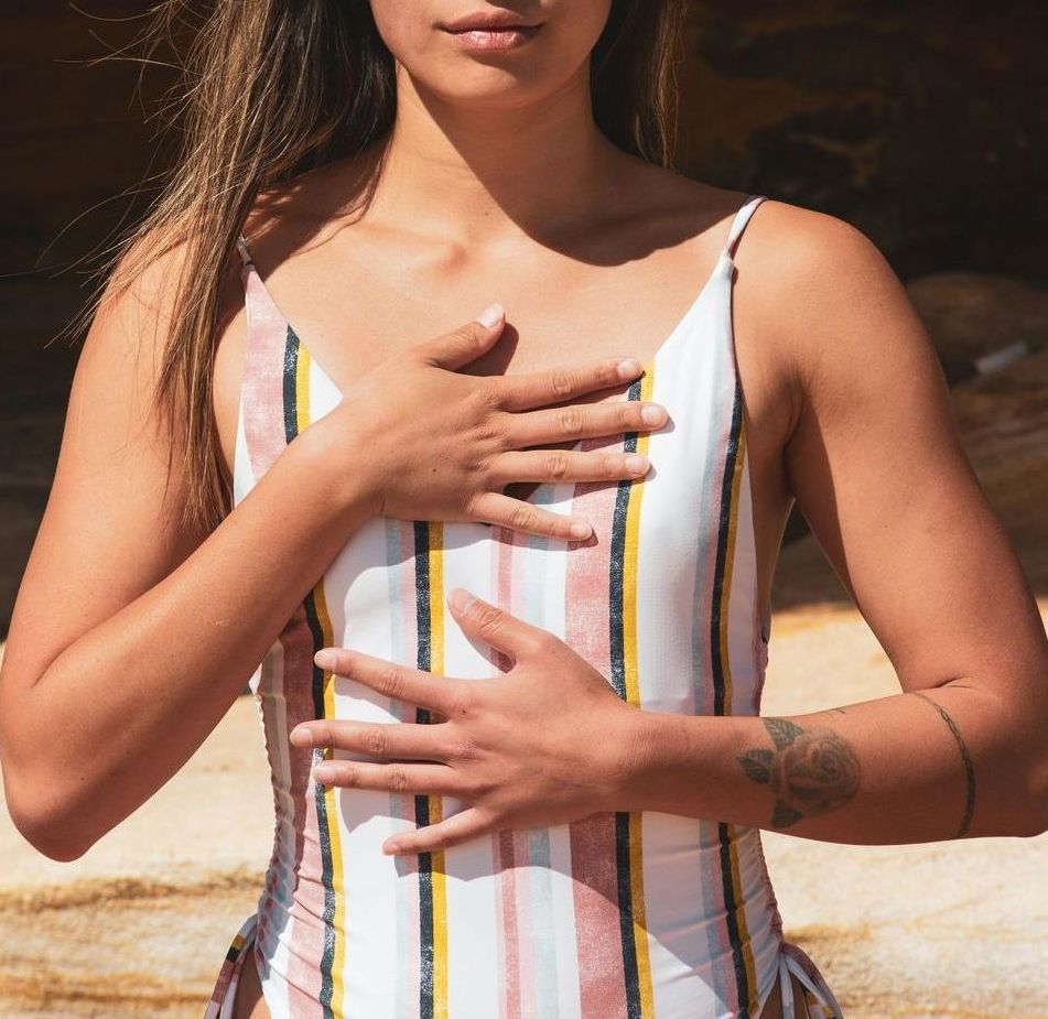 A woman in a striped swimsuit has her hands on her chest
