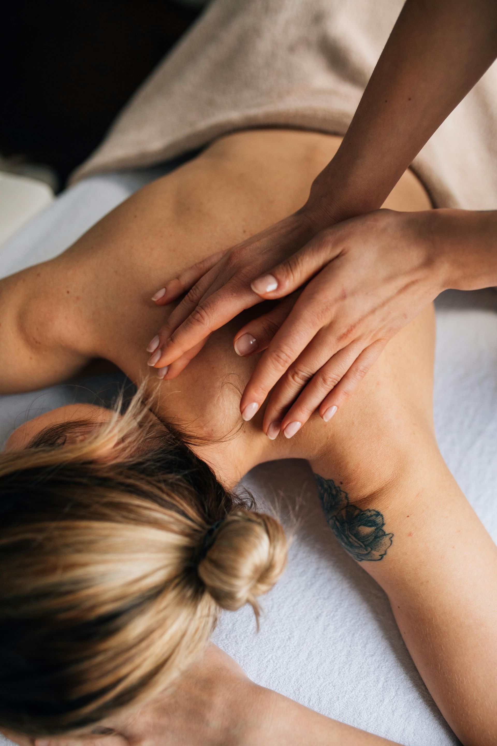 Person receiving a back massage on a massage table, hands kneading the shoulder and neck.