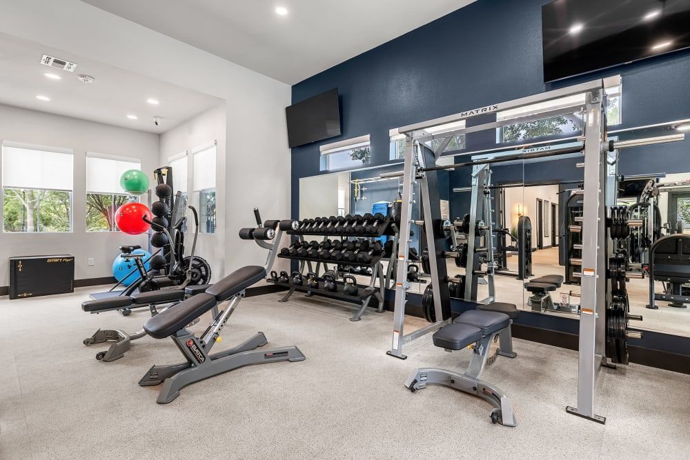 a gym with a lot of equipment and a large mirror at Marquis at Crown Ridge in San Antonio, TX.