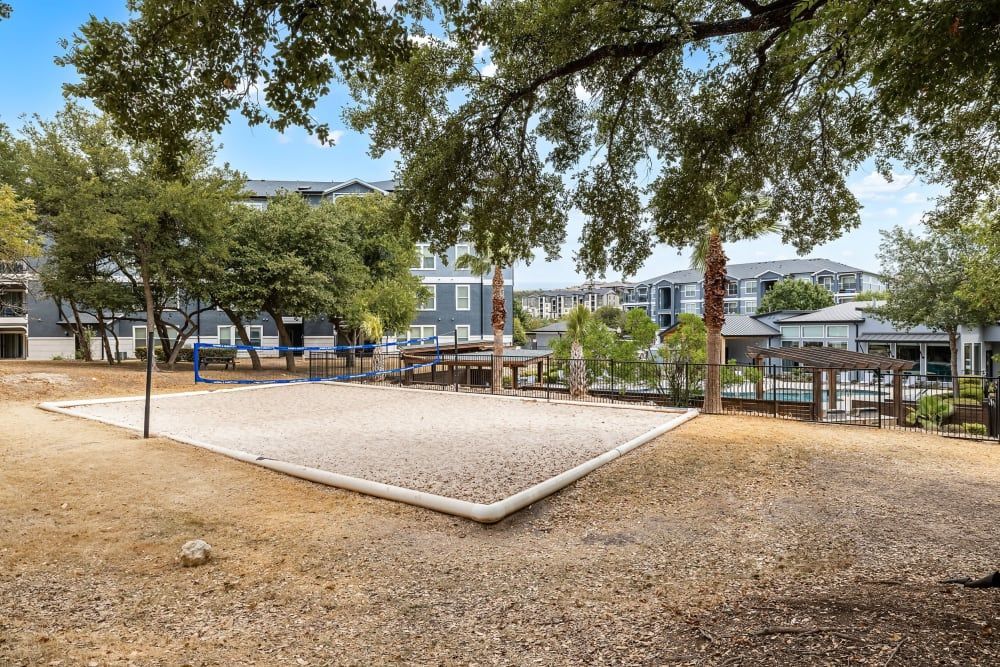 a volleyball court in a park with trees and buildings in the background at Marquis at Crown Ridge in San Antonio, TX.