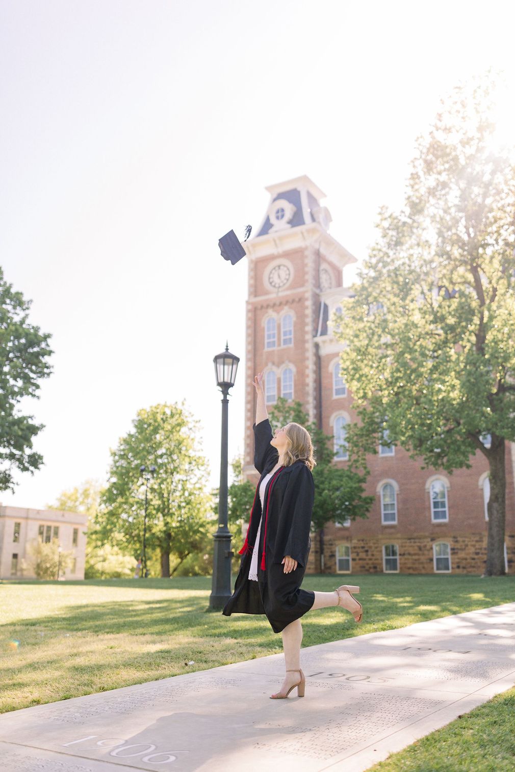 A woman in a graduation cap and gown is throwing her cap in the air.