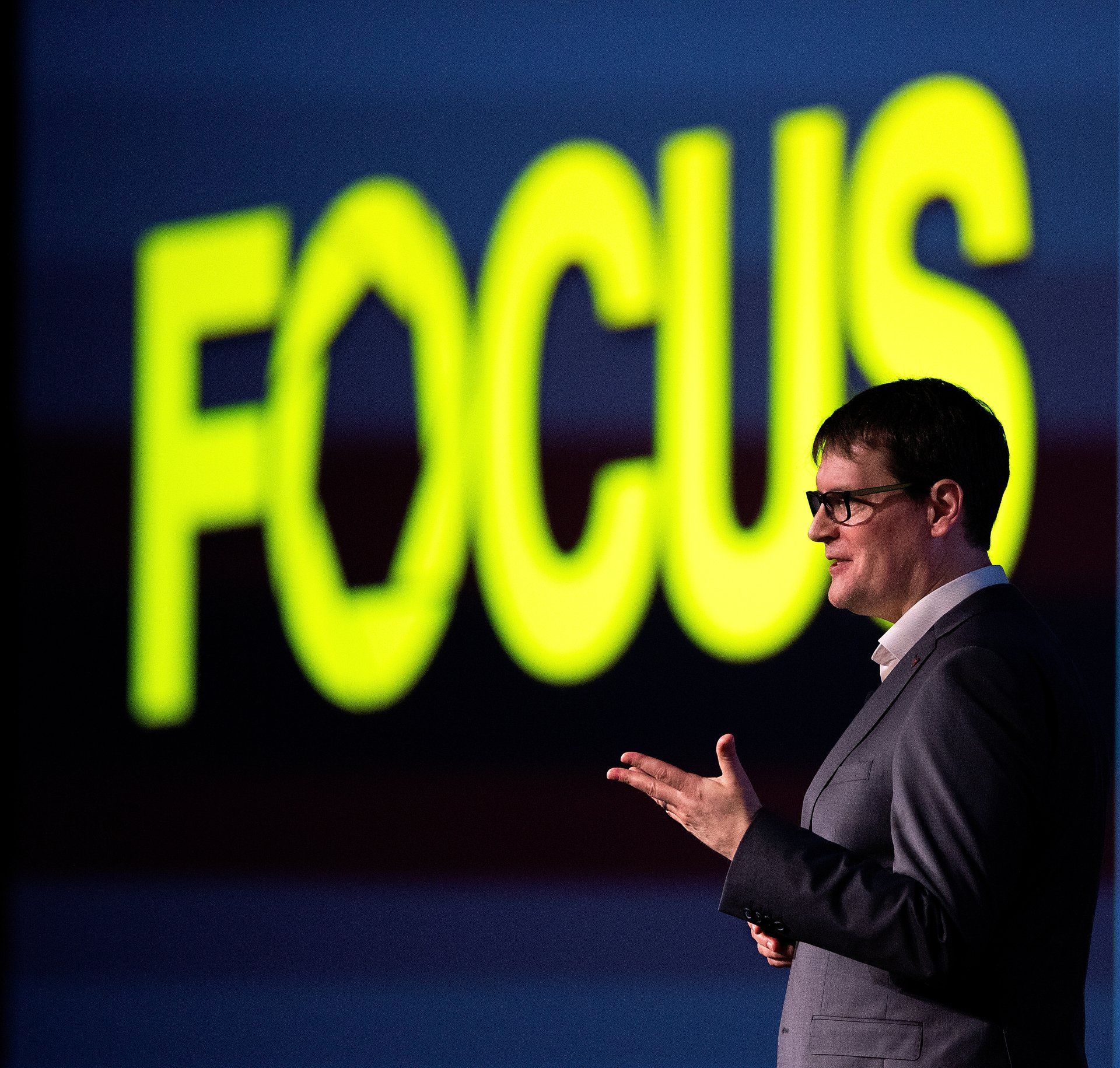 A speaker at a corporate event speaks in front of the word focus. 