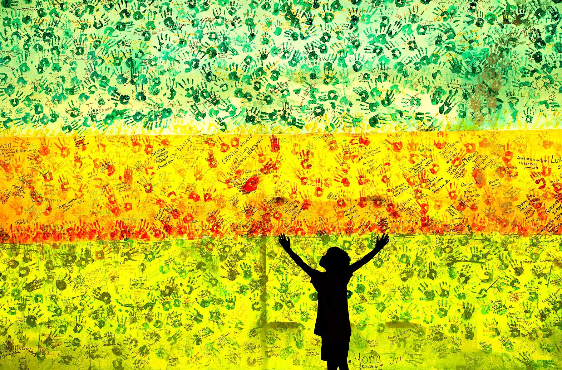 A child's silhouette in front of a colorful wall of hand prints