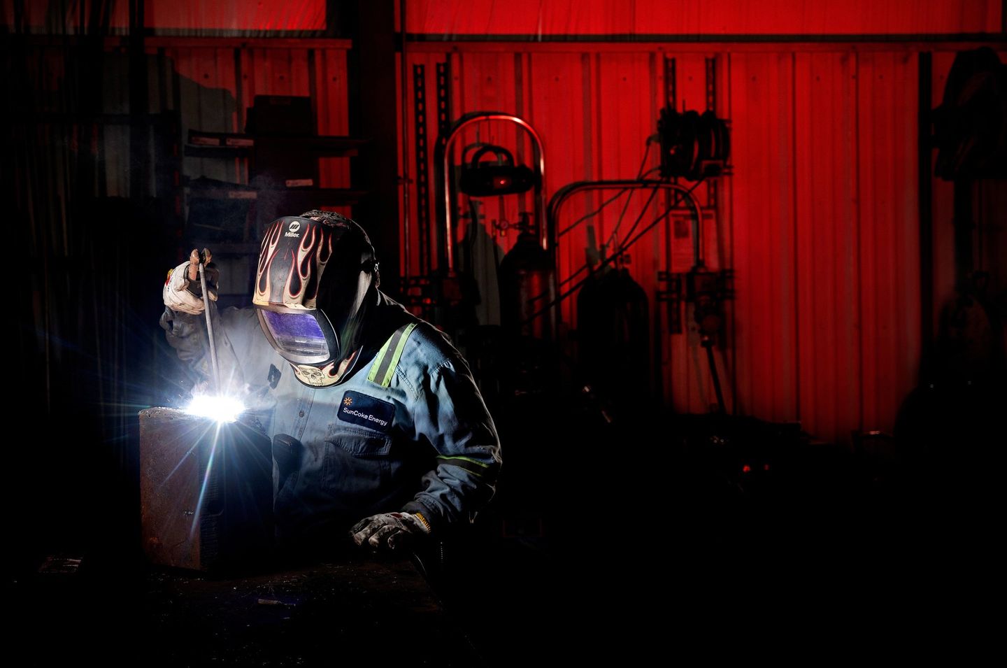 Photo shows a welder working in a facility. The welder is lit from the flame.