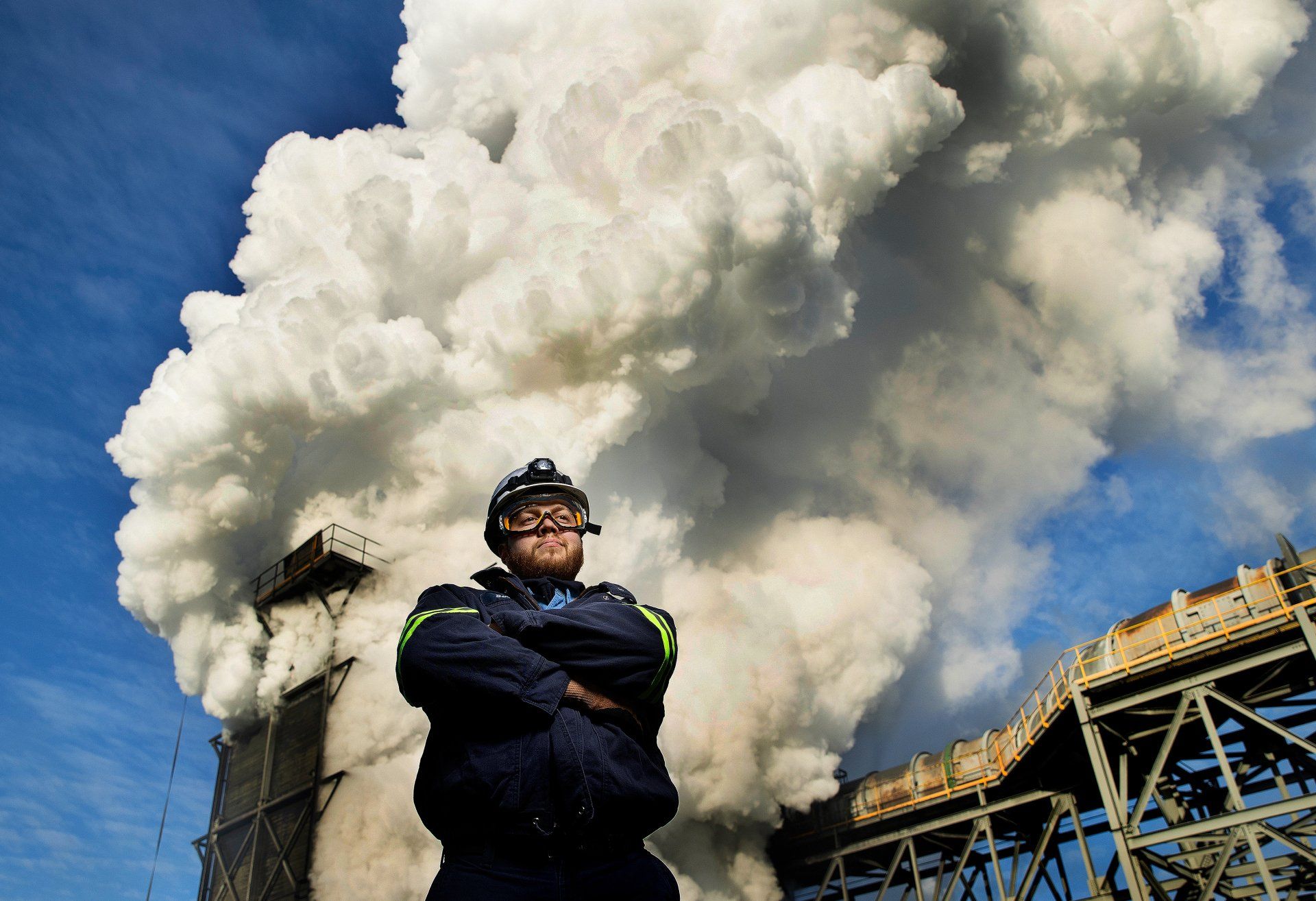 A worker at an industrial plant poses for a photo in front of a steam filled background. 