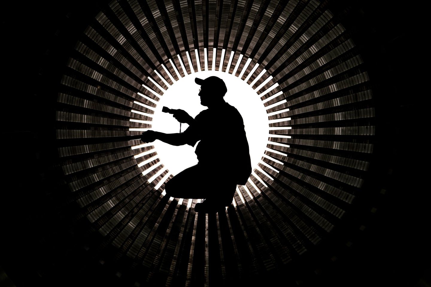 Photo shows the silhouette of an industrial mechanic working inside of a large turbine engine. The engine is still in the manufacturing facility. 
