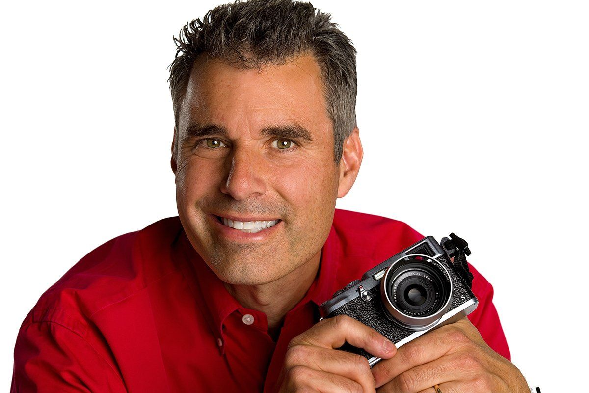 Man holding camera smiling at photographer.