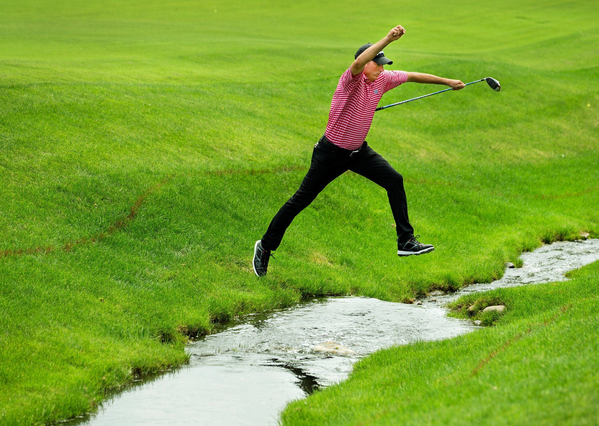 A golfer jumps a creek on the course of the Wells Fargo Championship