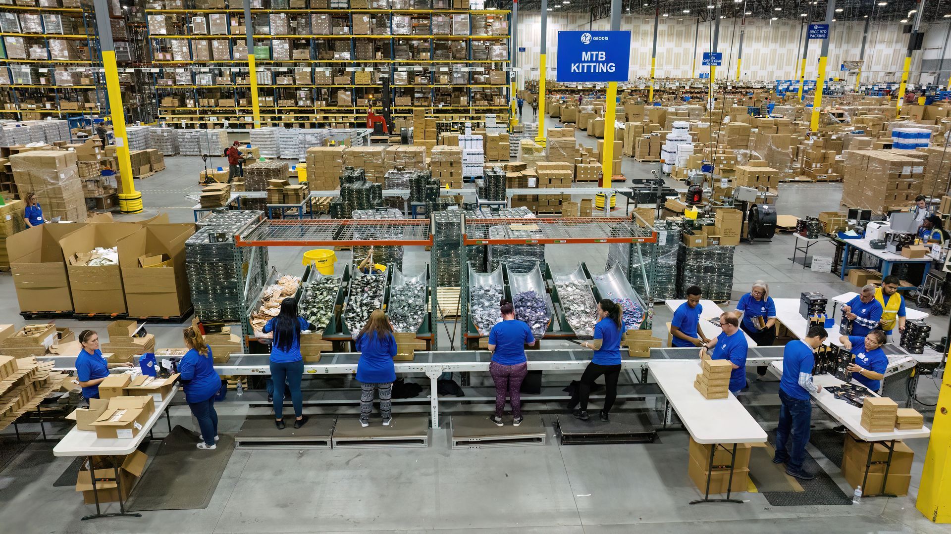 Workers package products into boxes that will be sent directly to consumers. The assembly operations are the last step in a long supply chain process. Photo used a drone inside the facility to show the size and scale of the operations. 