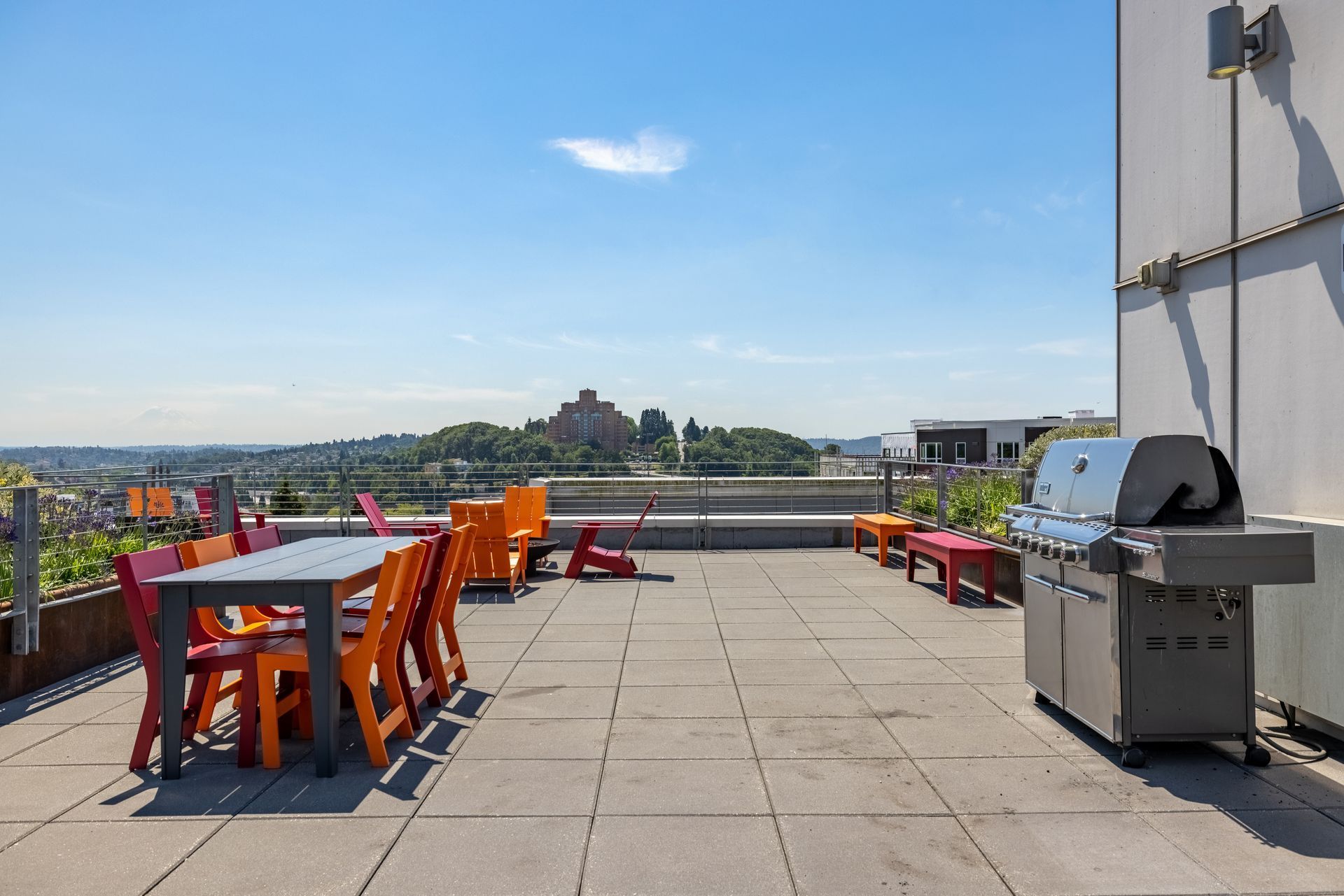 Rooftop terrace at dusk with colorful chairs around tables, decorative plants in planter boxes, and a serene view of the city skyline against a softly glowing sky at Anthem on 12th in Seattle, WA.