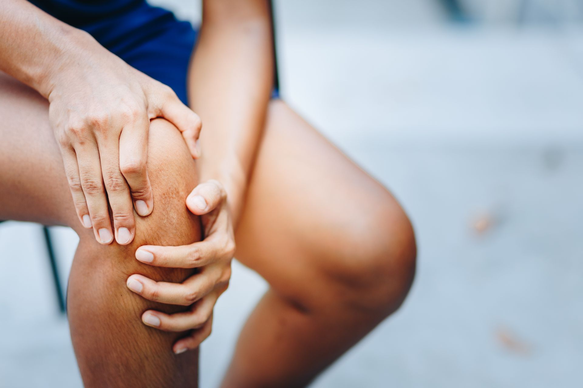 A woman is sitting on a chair holding her knee in pain.