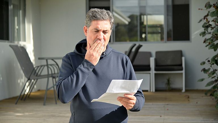 A man is holding a piece of paper in his hand and covering his mouth.