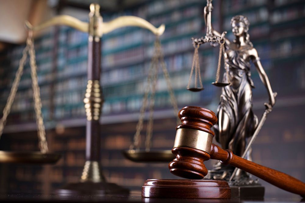 A statue of justice is sitting next to a judge 's gavel and scales of justice.
