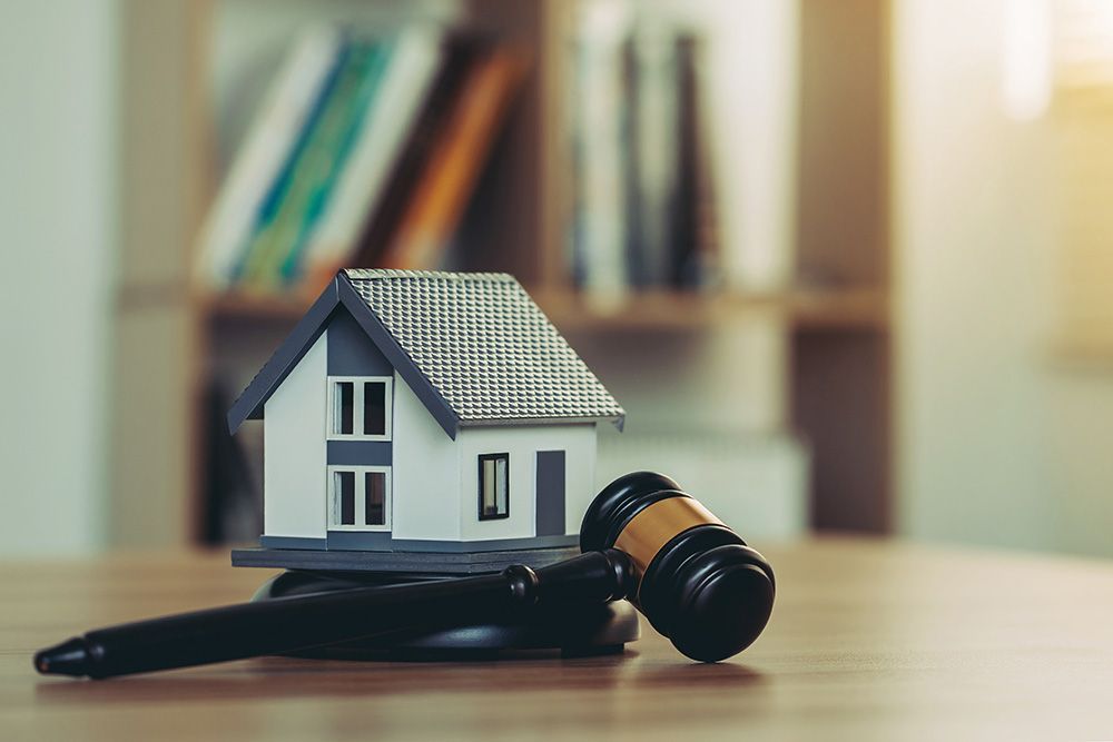 A model house is sitting on top of a wooden table next to a judge 's gavel.