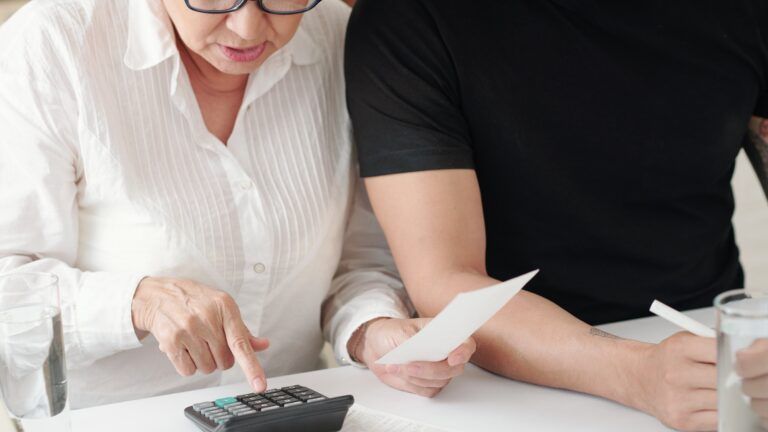 A man and a woman are sitting at a table using a calculator.