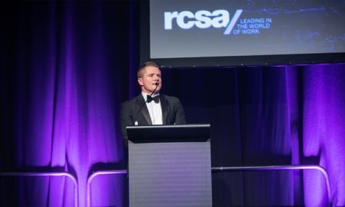 A man in a tuxedo is standing at a podium giving a speech.