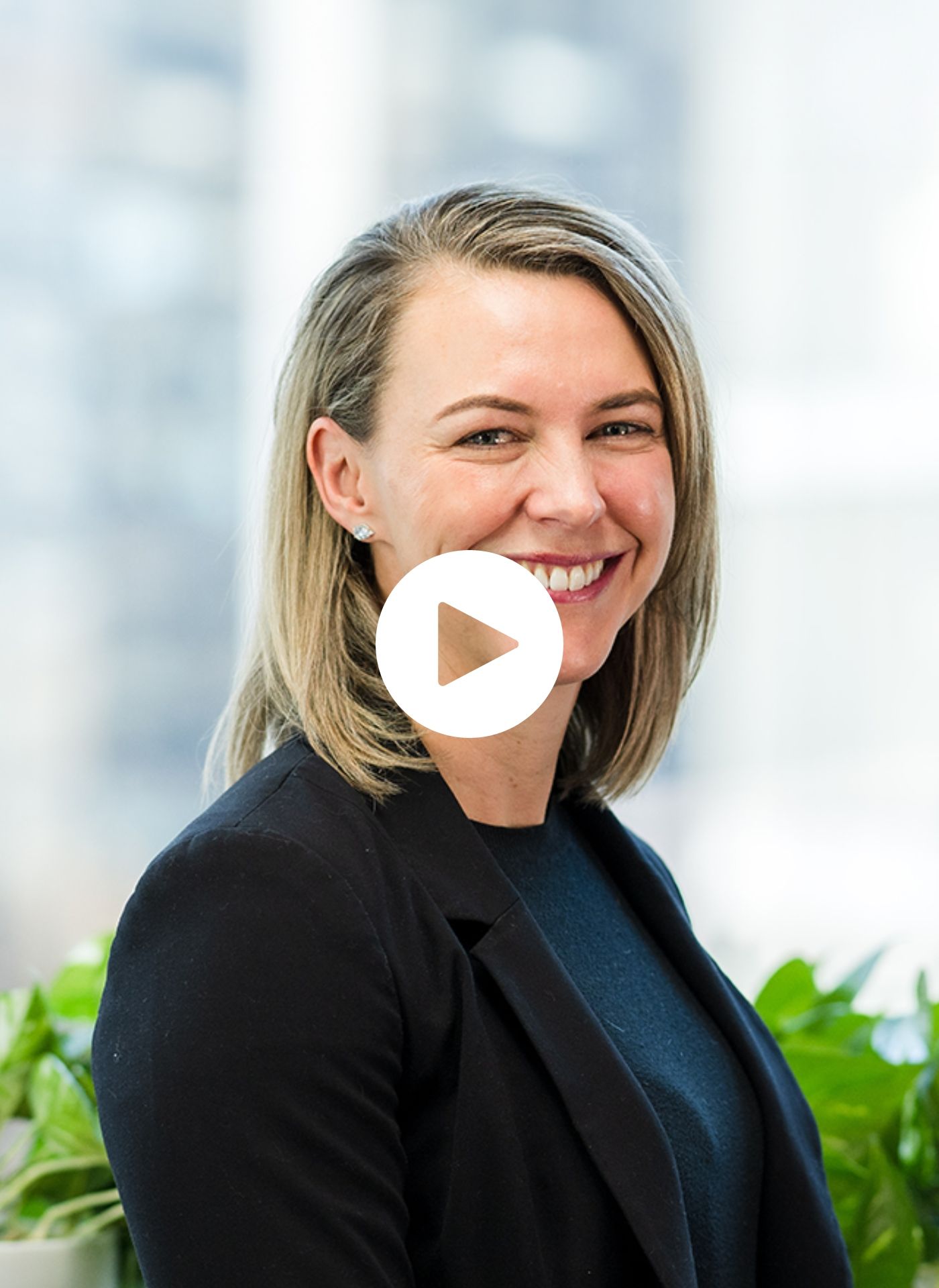 A woman in a black jacket is smiling with a play button on her face.