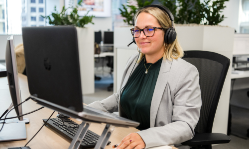 A woman wearing headphones is sitting at a desk in front of a computer.