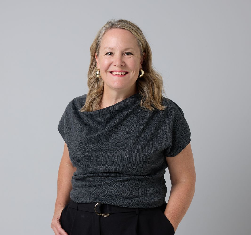 A woman wearing a blue cardigan and a plaid dress is smiling for the camera.