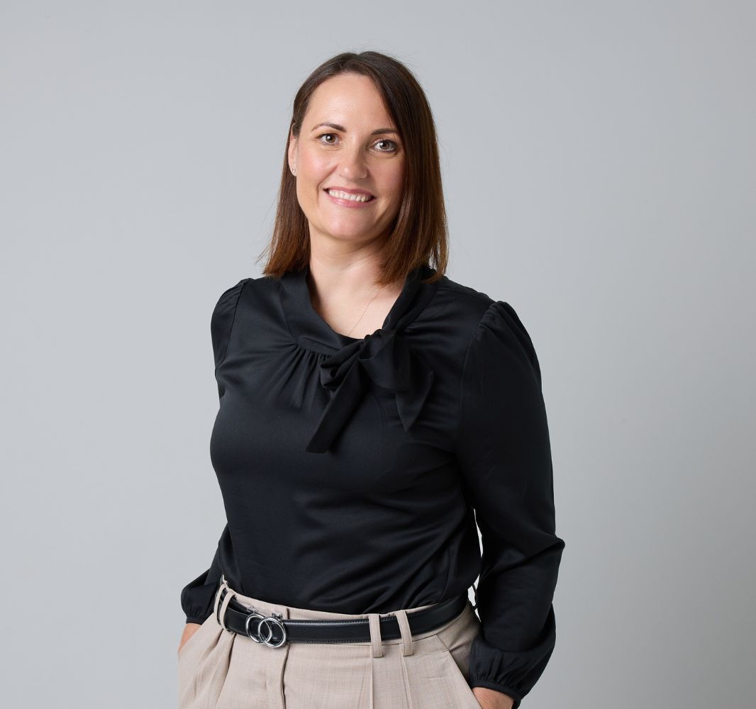 A woman in a blue dress is smiling with her hands in her pockets.