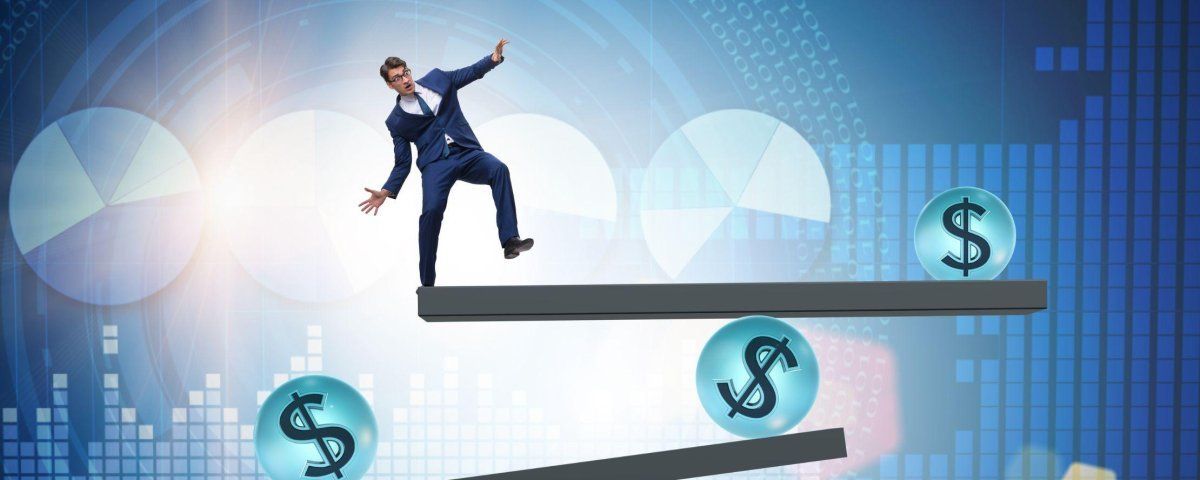 A man in a suit is balancing on a seesaw with dollar signs.