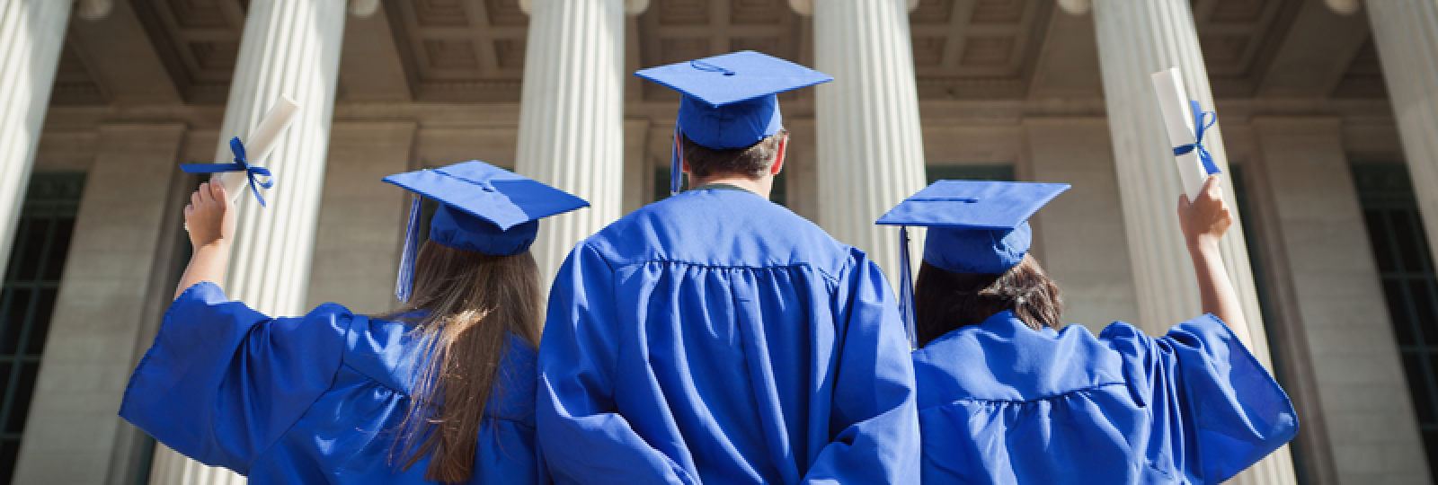 A group of graduates are standing in front of a building holding their diplomas.