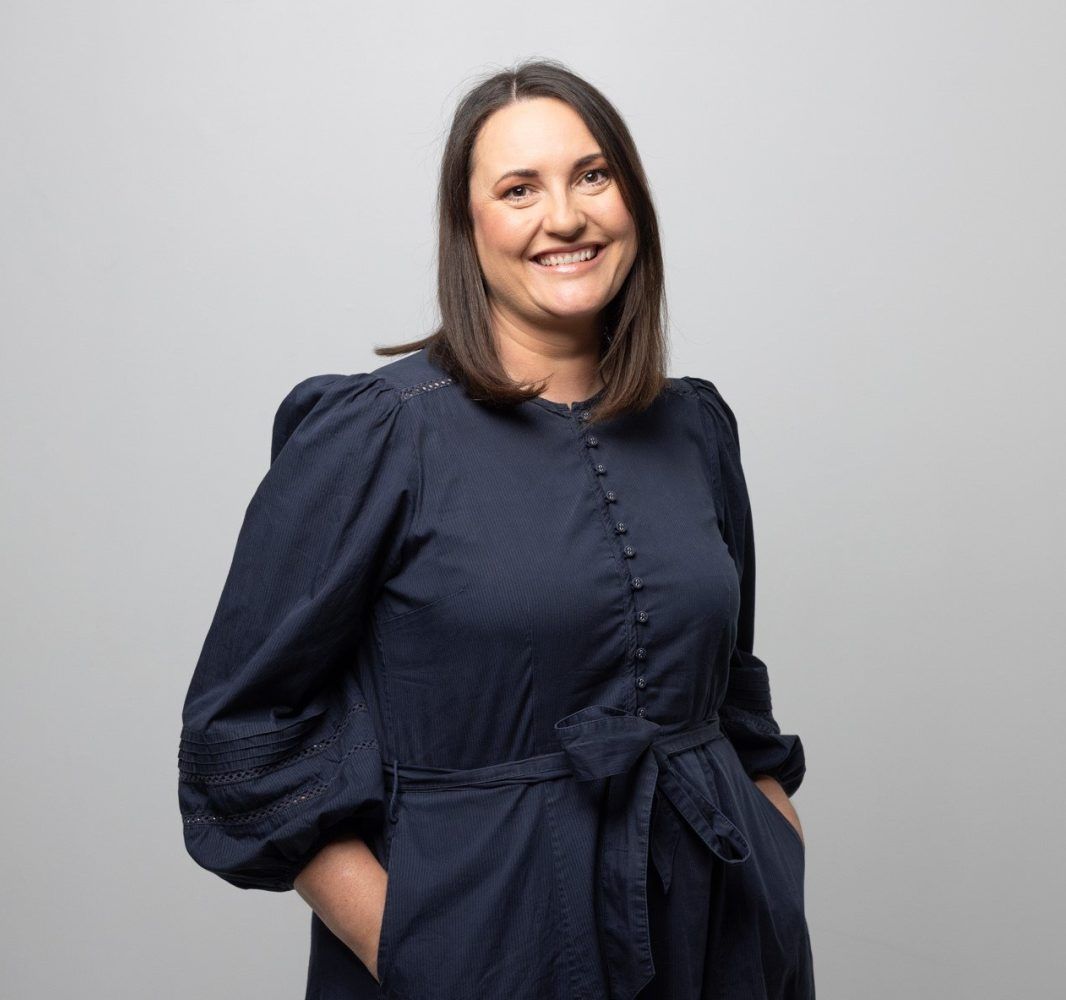 A woman in a blue dress is smiling with her hands in her pockets.