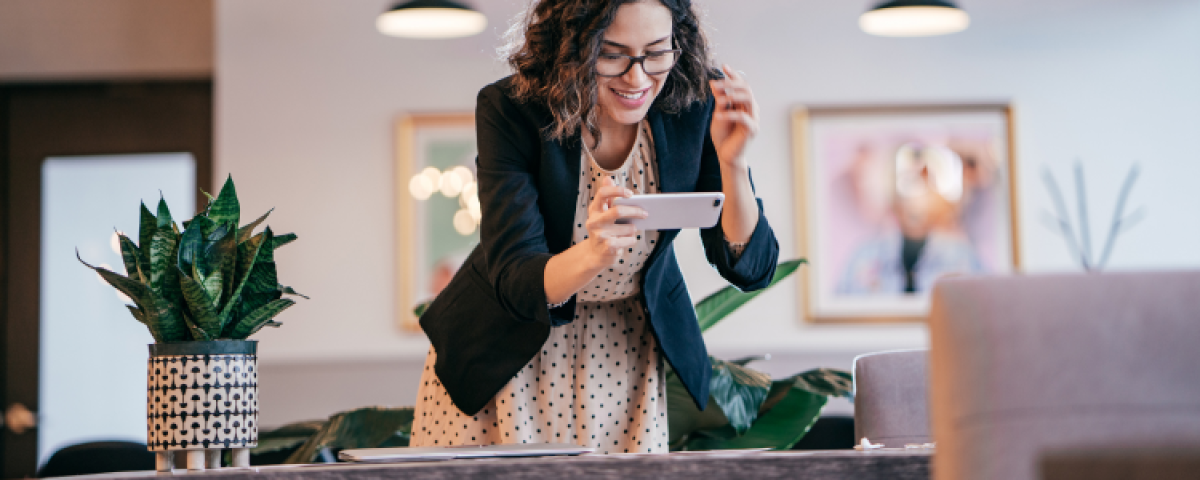 A woman is standing at a table looking at a cell phone.