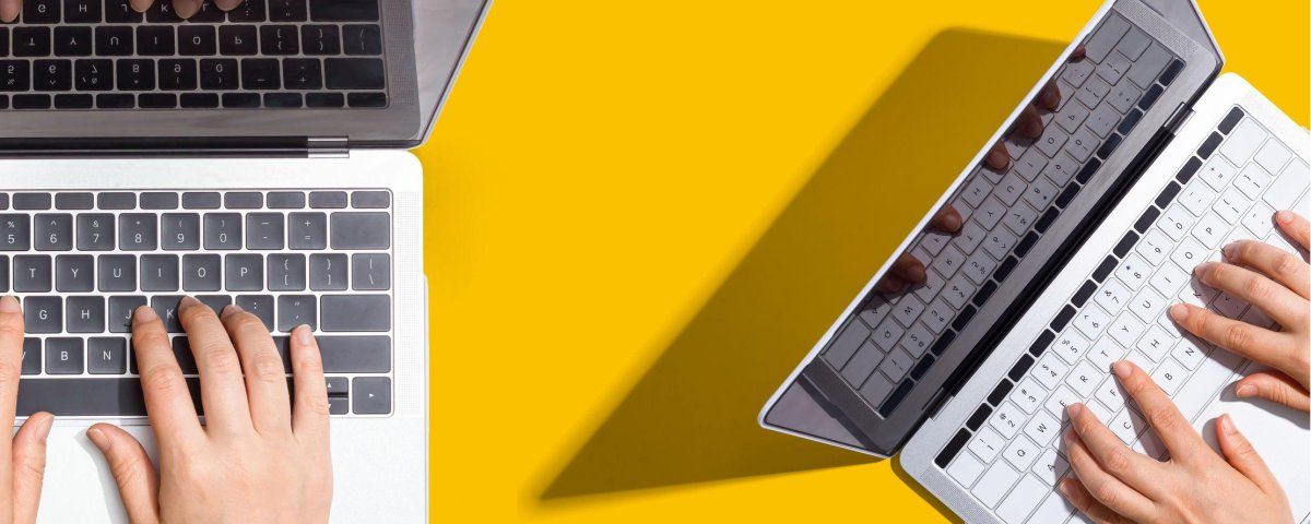 Two people are typing on two laptops on a yellow background.