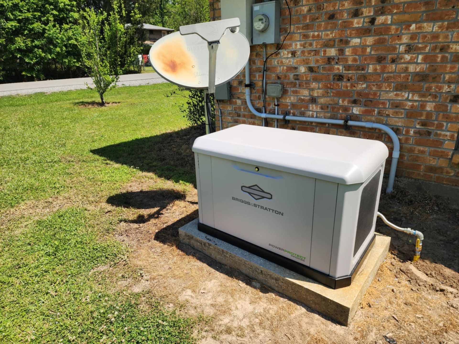 White backup generator beside a brick house with a satellite dish on a grassy lawn