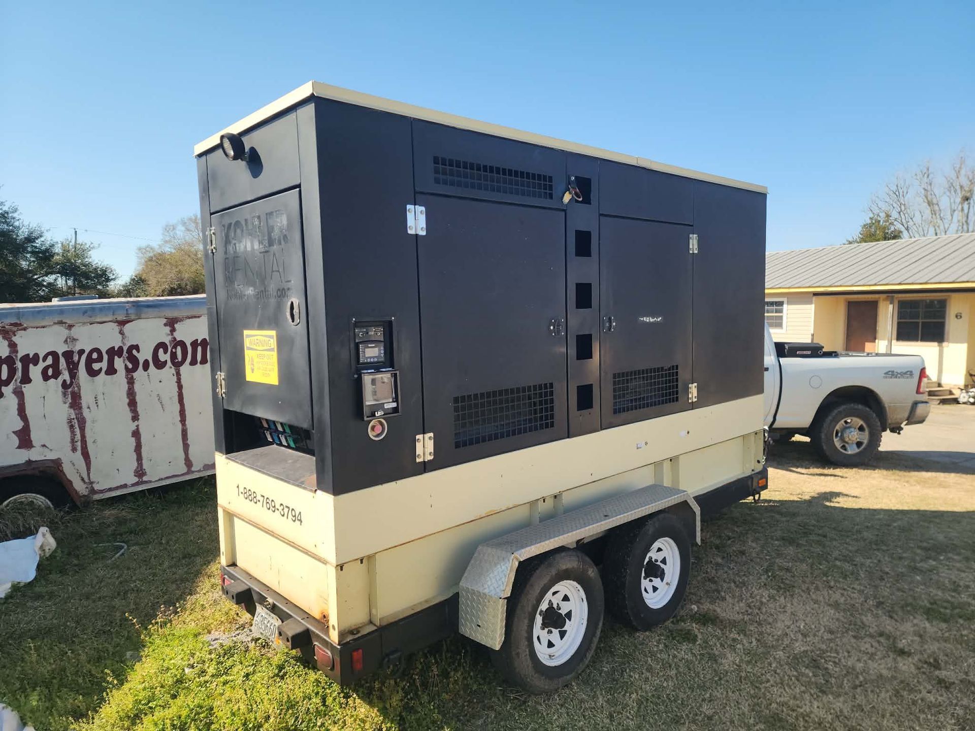 Beige trailer-mounted generator with black top parked on grass beside a white pickup truck