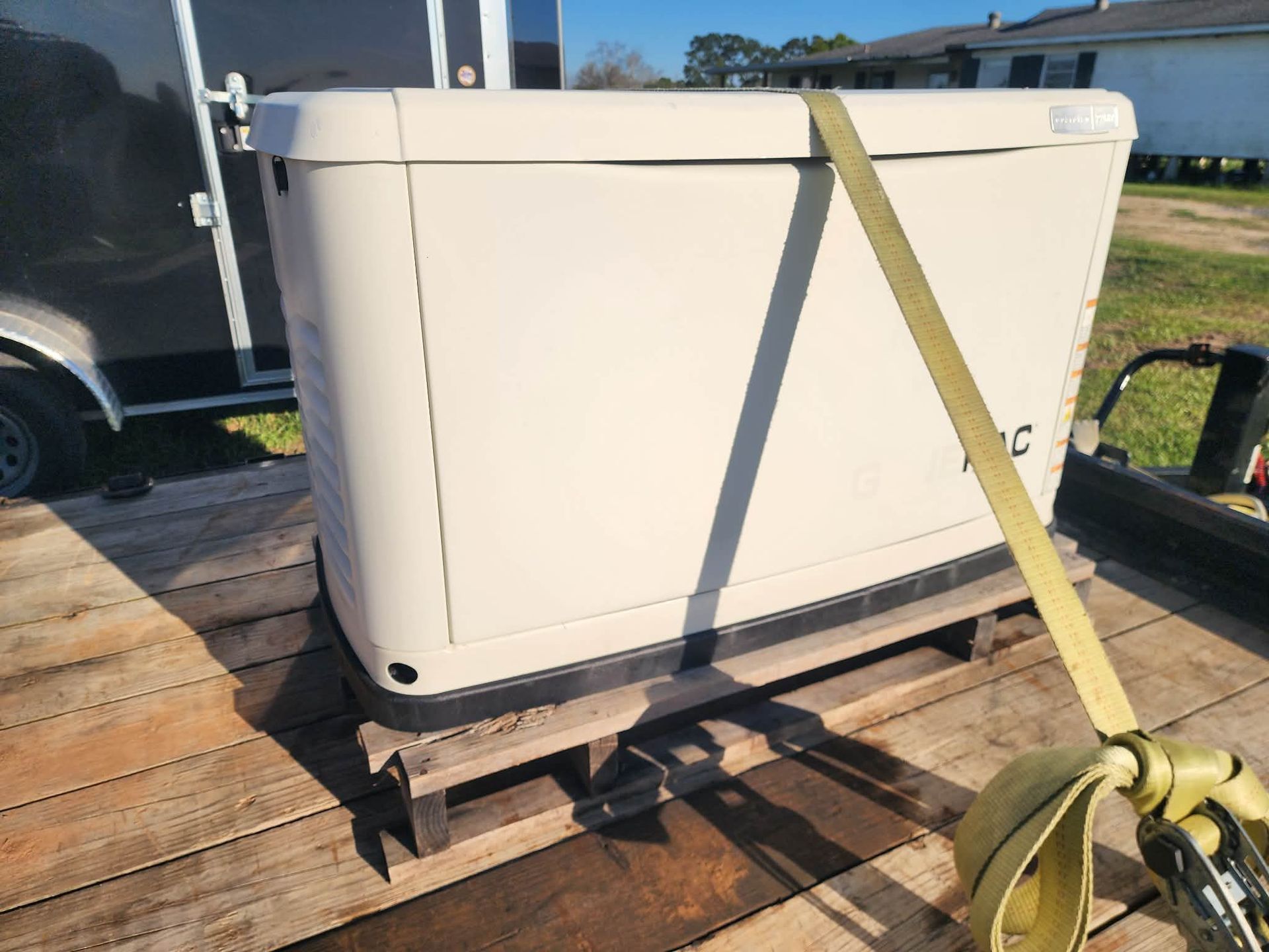 White hot tub strapped to a wooden pallet outdoors beside a trailer.