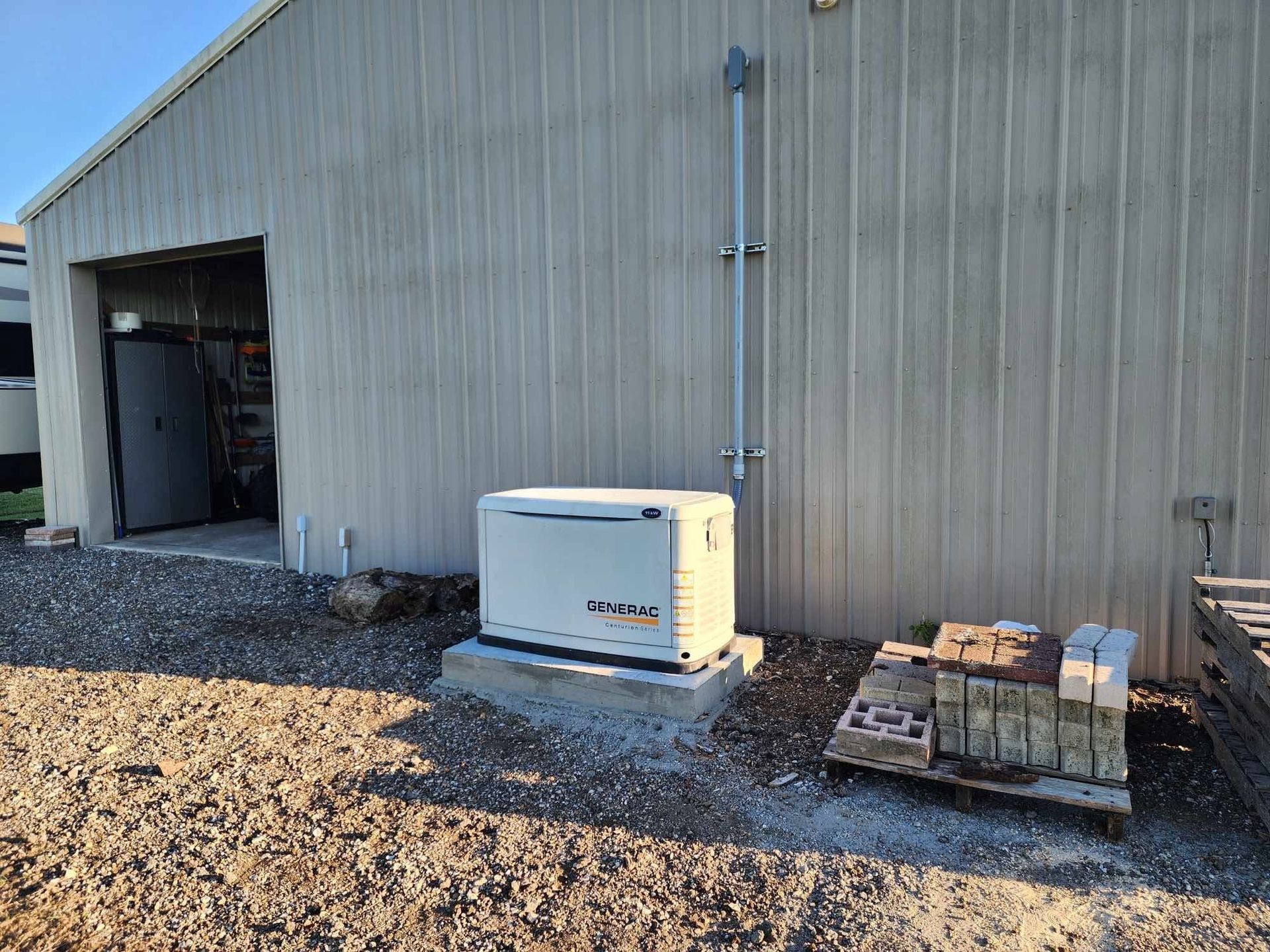 Industrial building exterior with a white generator, open bay door, and pallets on gravel.